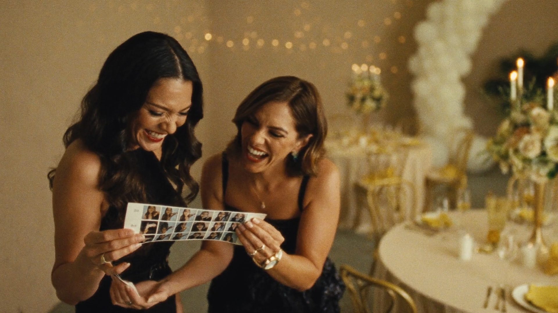 Two wedding guests laughing over a freshly printed photo booth strip at an elegant Phoenix reception